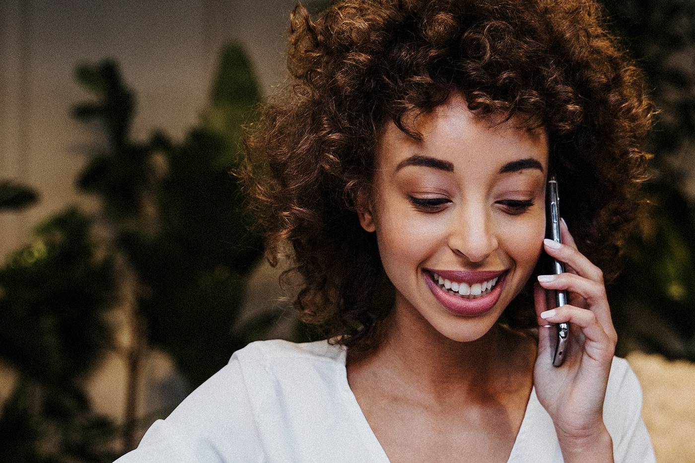 A smiling woman with curly hair is talking on a smartphone.