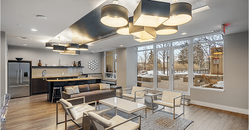 A modern lounge area featuring a comfortable seating arrangement with a sofa, chairs, and small tables, illuminated by stylish light fixtures.