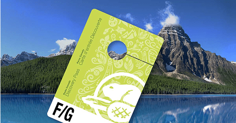 A green Discovery Pass card in front of a scenic mountain landscape with a lake and forest.
