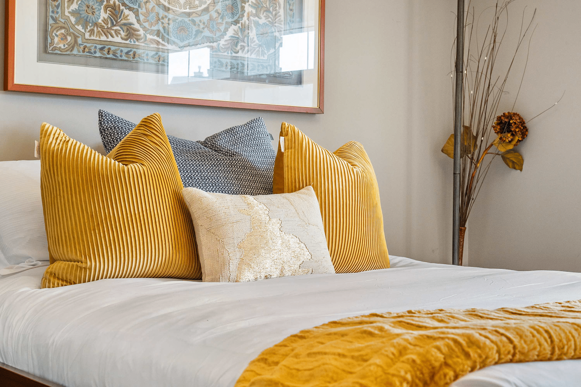 A stylish bed with multiple decorative pillows in yellow and blue hues, a textured yellow throw blanket, and a minimalist decor style.